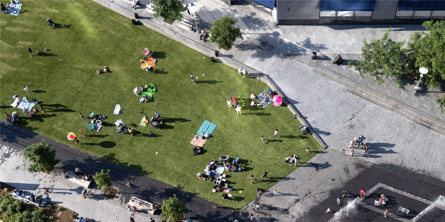 Aerial view of an urban park with people enjoying a sunny day on patches of grass surrounded by walking paths.