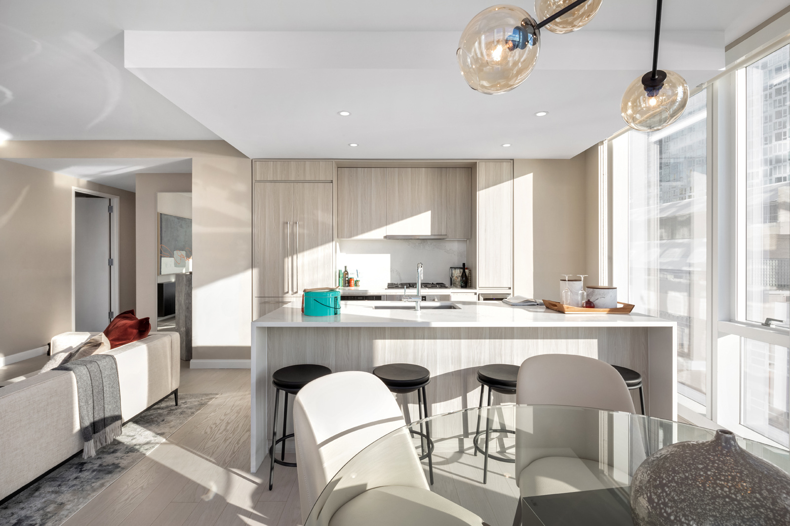 Modern, sunlit kitchen with a central island, sleek cabinetry, and a glass dining table, complemented by stylish bar stools and unique pendant lights.