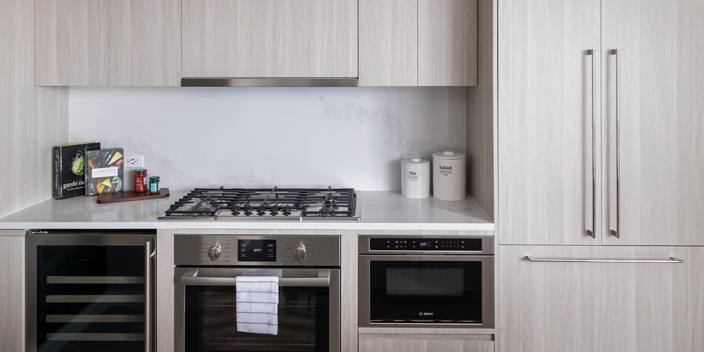 A sleek modern kitchen featuring stainless steel appliances, including a gas stove, oven, and microwave, with white minimalist cabinetry and subtle decorative elements.