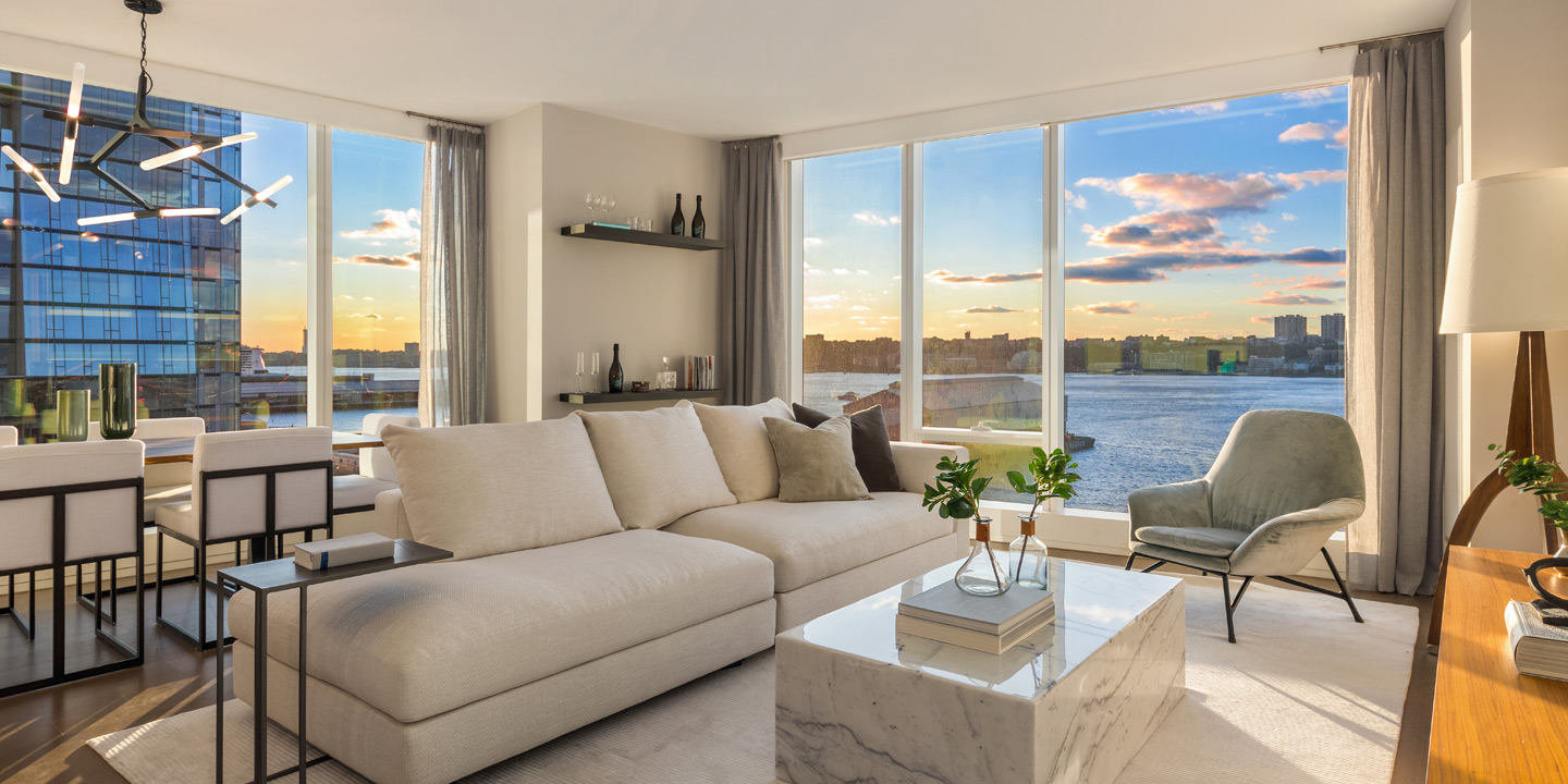 Modern living room with large windows offering a panoramic view of the city skyline during sunset, featuring stylish furniture and a warm, inviting ambiance.