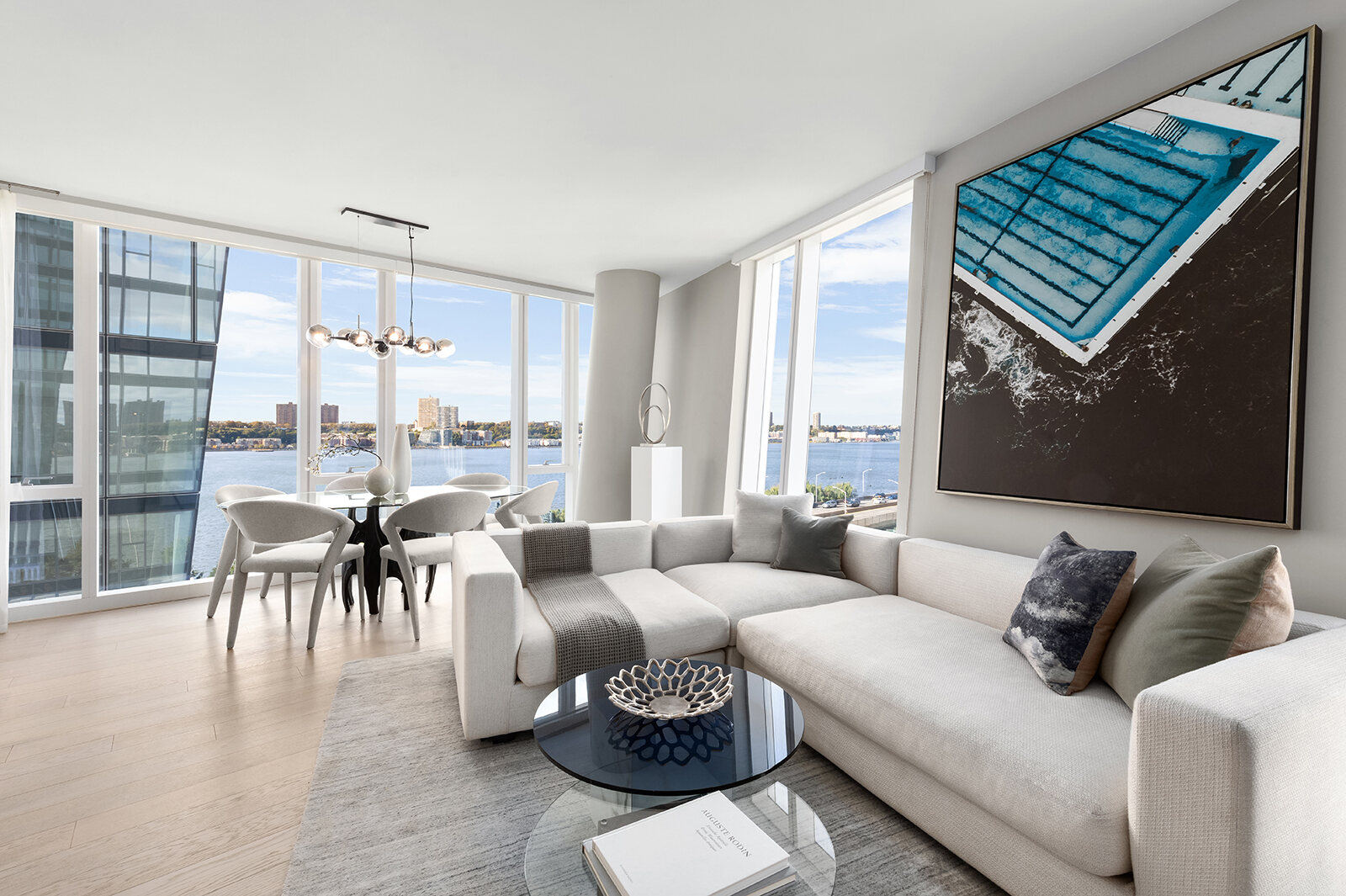 Modern urban living room with expansive windows offering a panoramic city view, adorned with a large artwork of a pool and furnished with a stylish sectional sofa and elegant dining area.