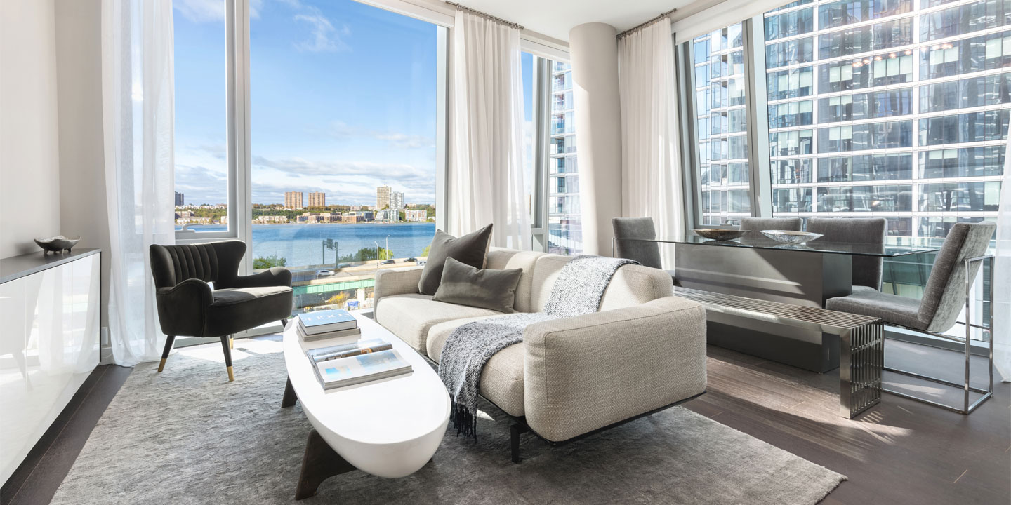 Modern urban living room with a panoramic view of a city waterfront, featuring stylish furniture, floor-to-ceiling windows, and abundant natural light.