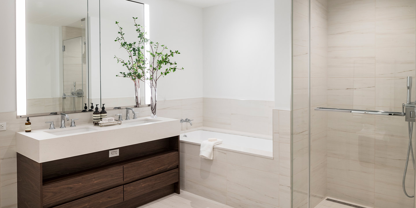 Modern bathroom interior with a sleek wooden vanity, clean white countertops, a large mirror, and a glass-enclosed shower-tub combo, accented by a vase with green branches for a touch of nature.