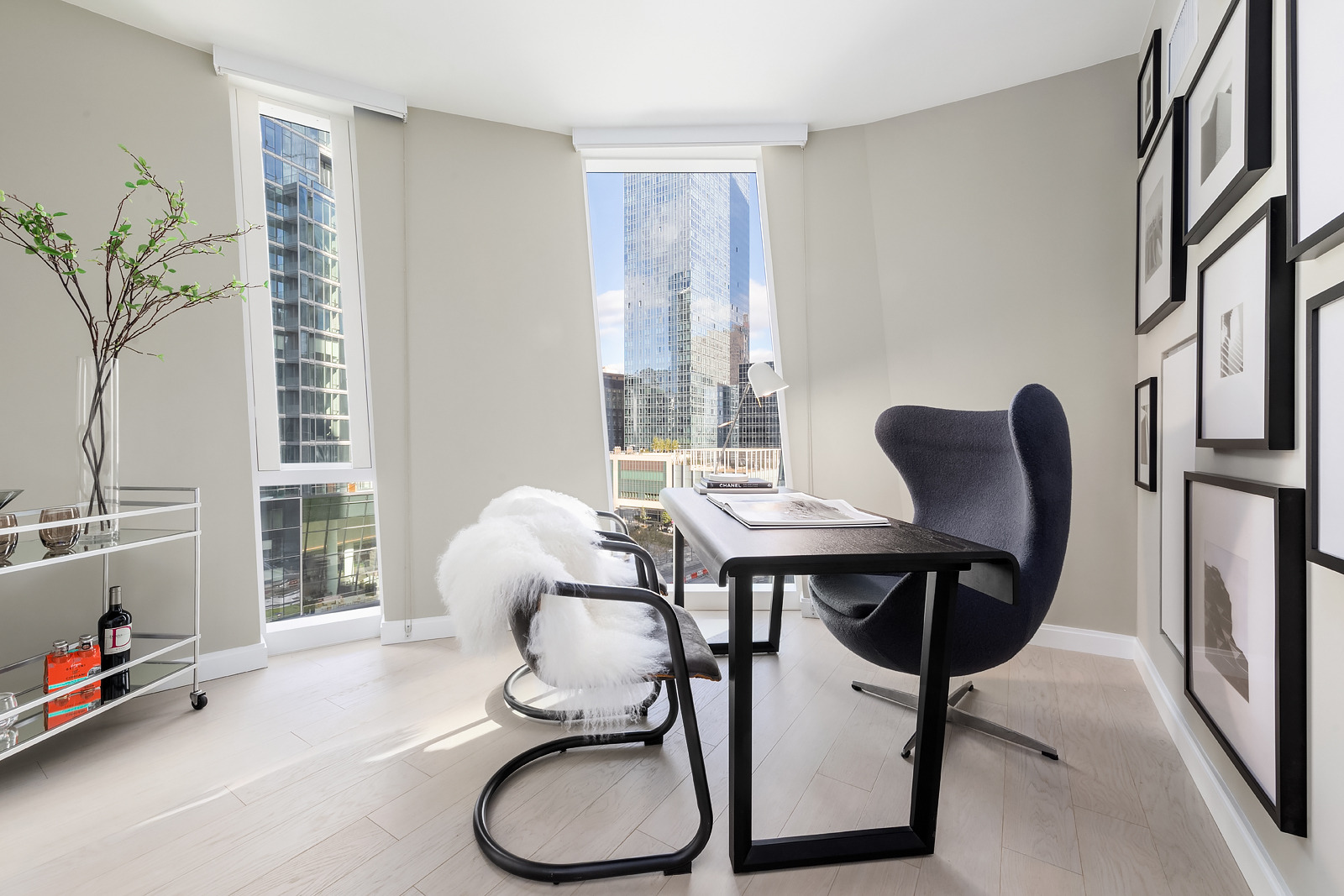Modern home office with sleek furniture and floor-to-ceiling windows offering an urban view.