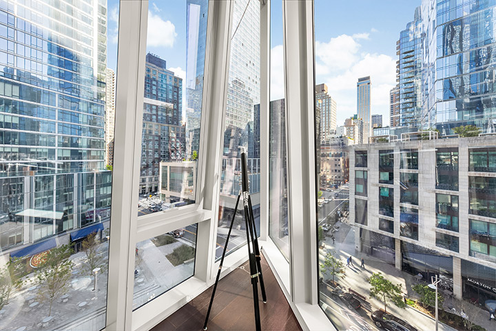 Urban oasis: a bright corner room with floor-to-ceiling windows offering a panoramic view of a bustling cityscape and skyscrapers under a clear blue sky.