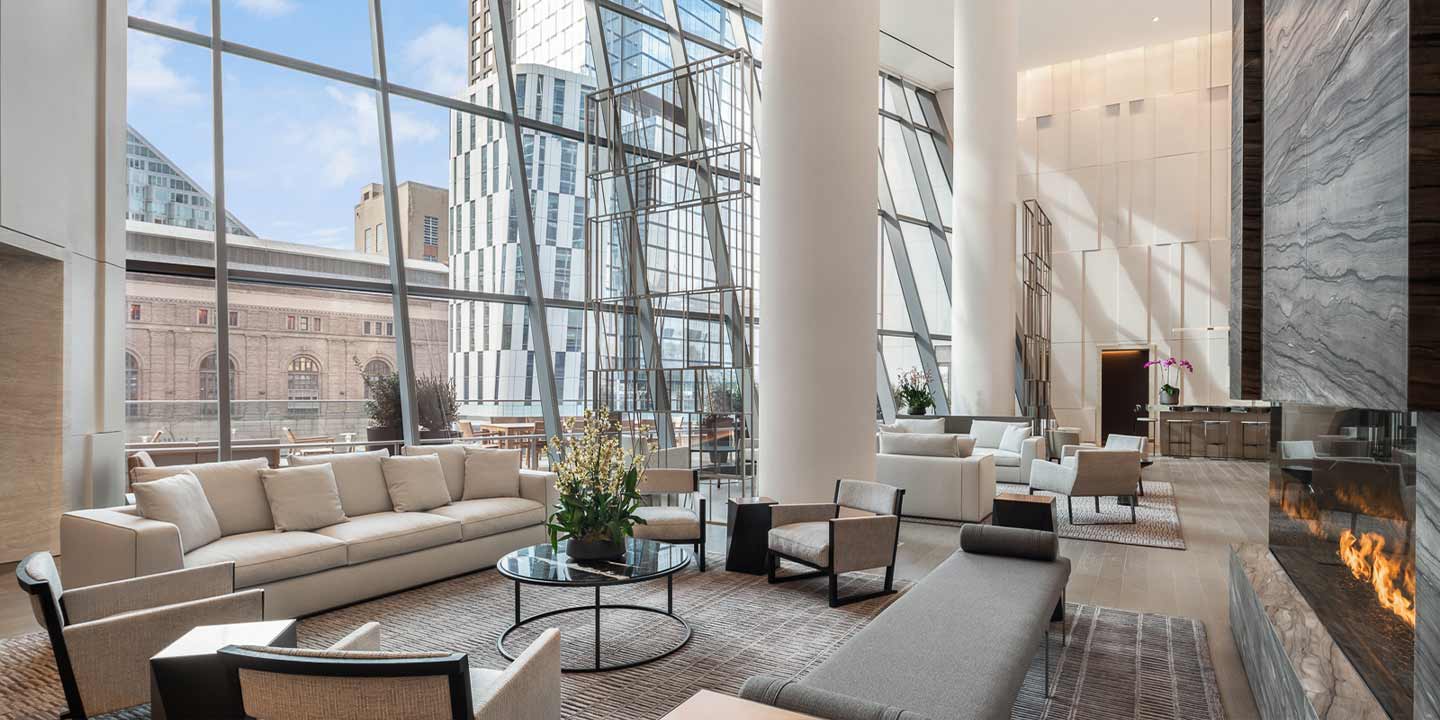 Modern and elegant hotel lobby with floor-to-ceiling windows overlooking the city, featuring plush seating areas and a cozy fireplace.