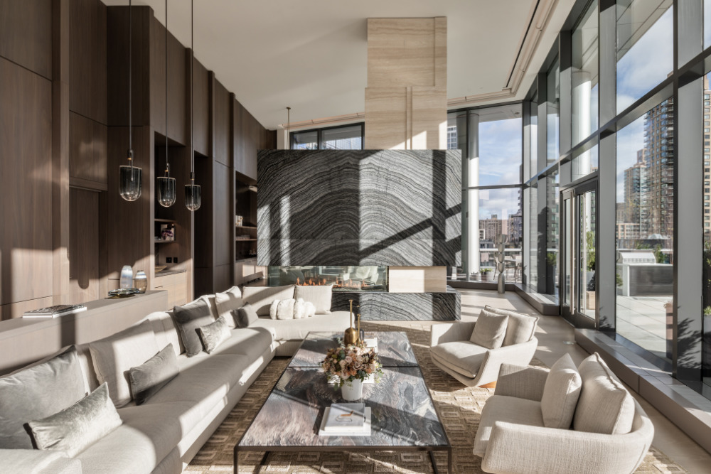A luxurious, modern living room bathed in natural light featuring a large marble statement wall, floor-to-ceiling windows, and elegant neutral-toned furniture.