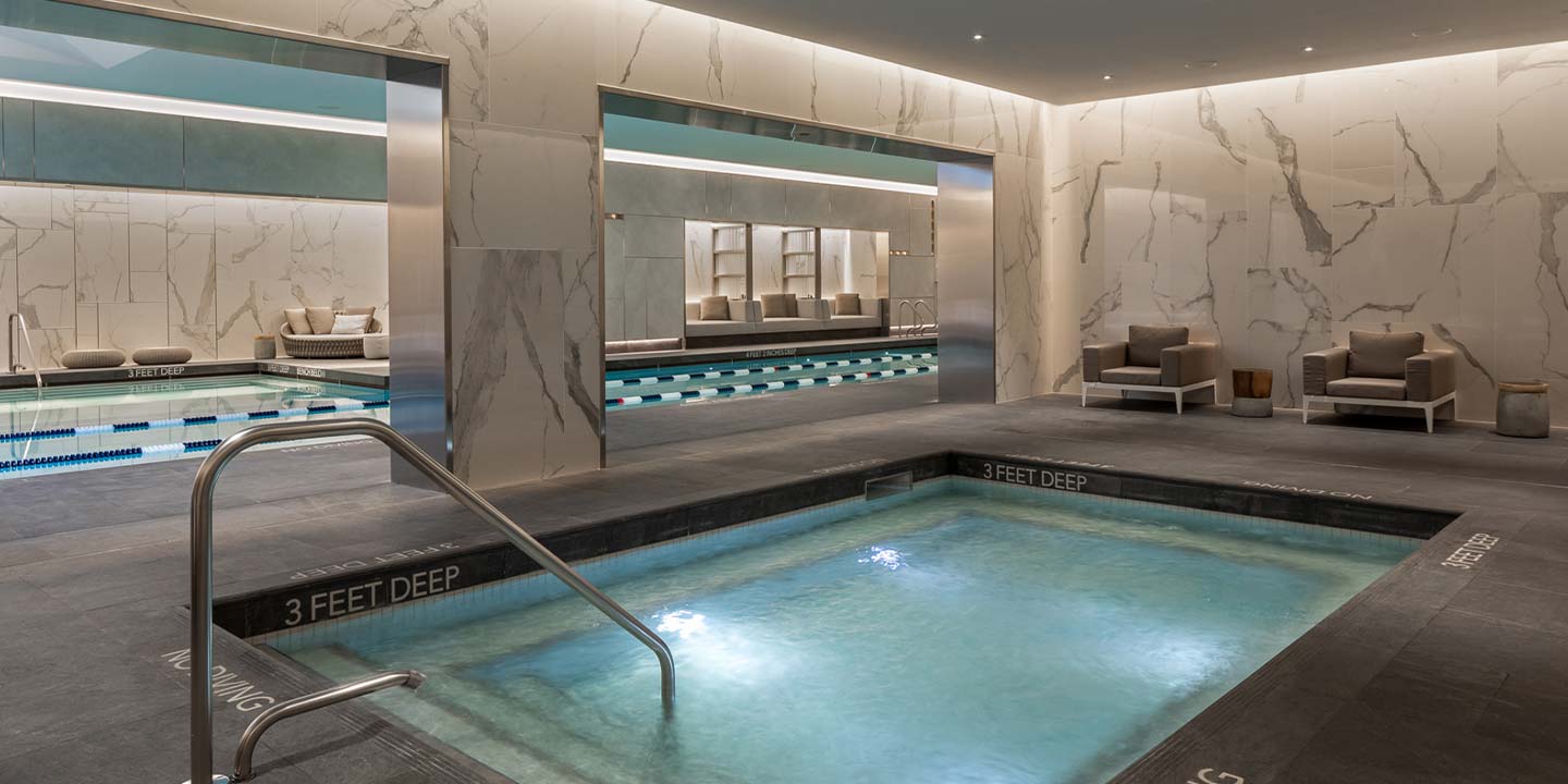 Modern luxury spa with an inviting hot tub and tranquil relaxation area, characterized by elegant marble accents and serene blue lighting.
