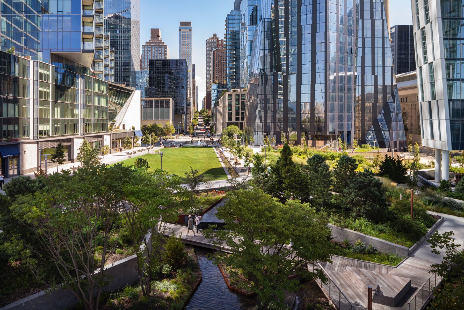 Modern urban park nestled between sleek high-rise buildings, offering a green escape with walking paths, seating areas, and lush landscaping in the heart of a bustling city.