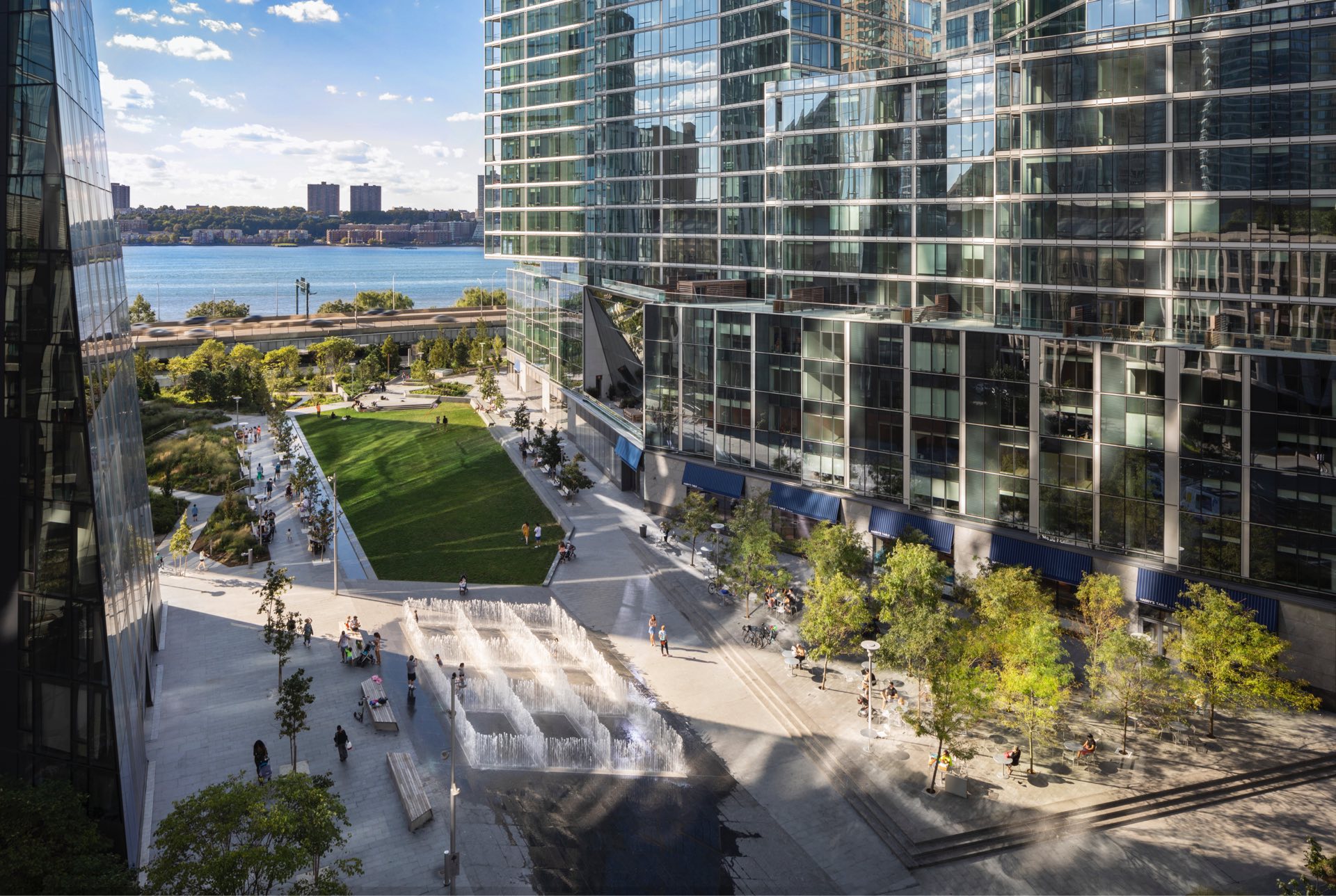 Modern urban oasis: a bustling cityscape with contemporary glass buildings framing a vibrant public space, where people enjoy the sunny outdoors against a backdrop of calming waterfront views.
