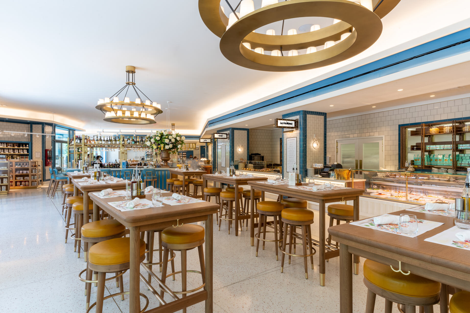 An elegant and spacious diner-style restaurant with retro-inspired design, featuring a central bar with stool seating, circular chandeliers, and a bright, welcoming ambiance.