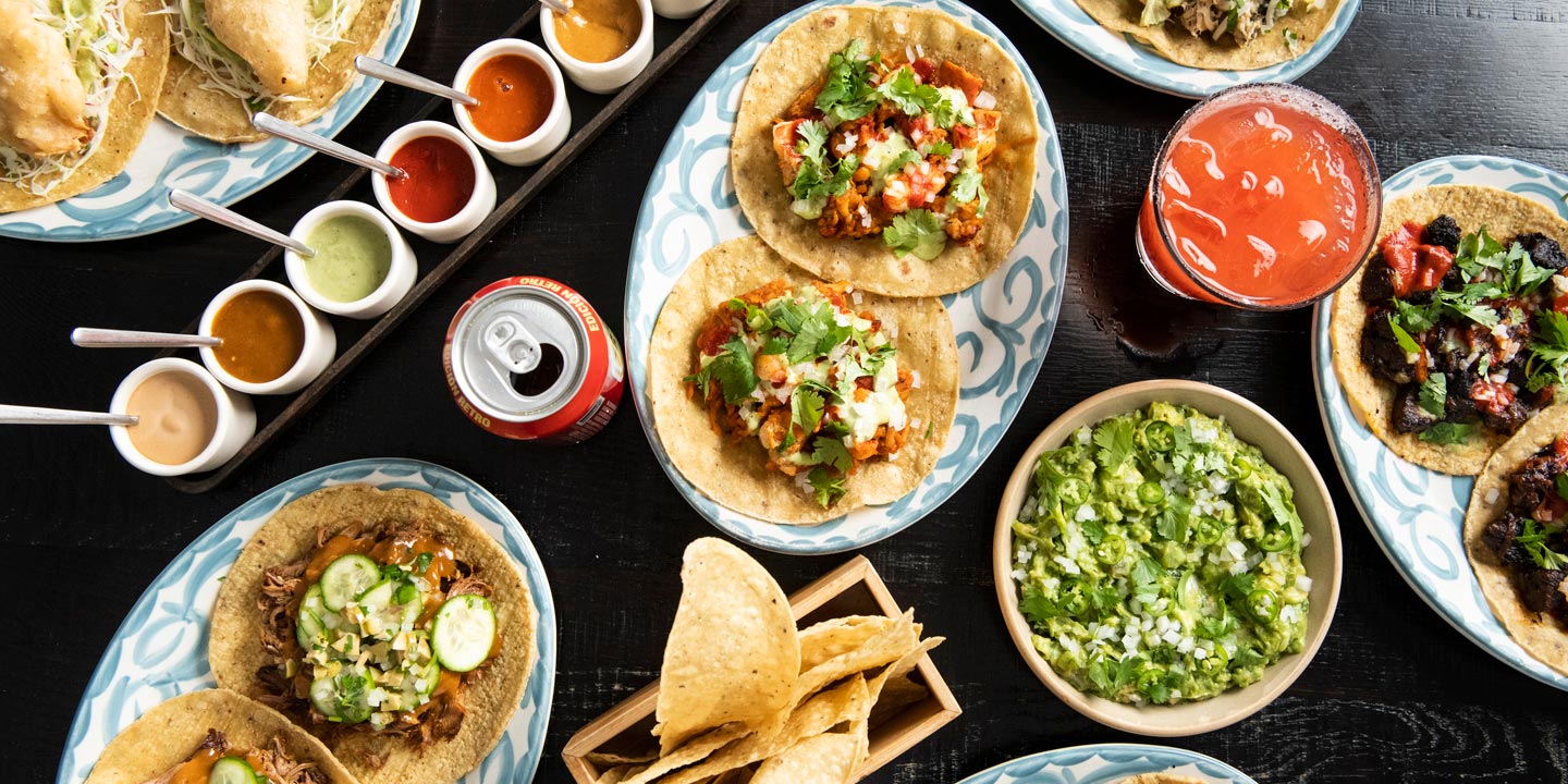 A vibrant array of mexican food, featuring an assortment of tacos, salsas, guacamole, and a refreshing beverage, perfectly laid out for a festive feast.