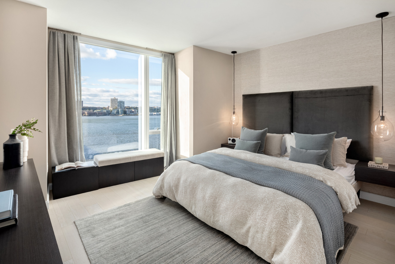 Modern and cozy bedroom with a luxurious bed and a stunning view of the river through large windows, bathed in natural light.