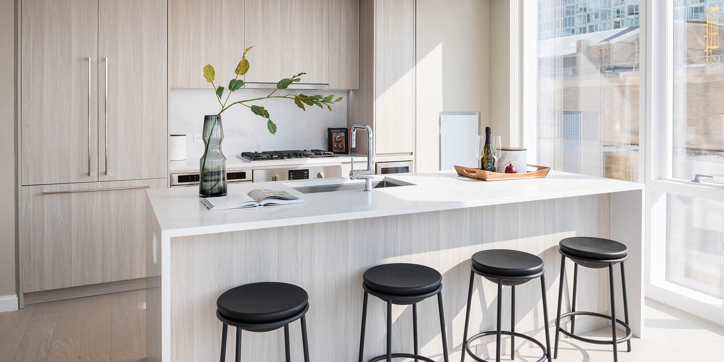 Modern and bright kitchen with clean lines, featuring a white countertop island, black bar stools, and large windows offering plenty of natural light.